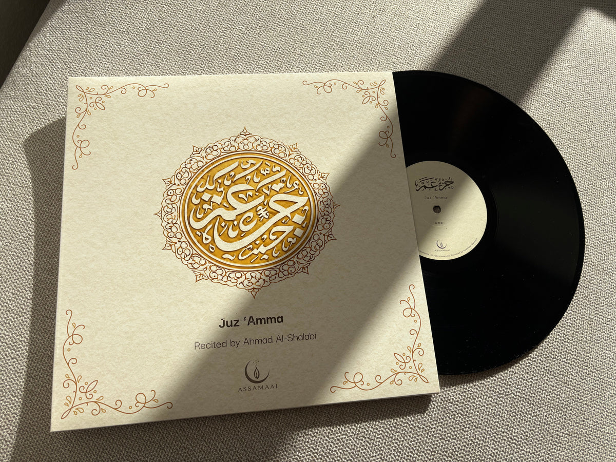 A vinyl record partially pulled from a cream-colored sleeve with ornate gold Arabic calligraphy and decorative corner flourishes. The sleeve reads 'Juz Amma' and 'Recorded by Ahmad Al-Sheikh.